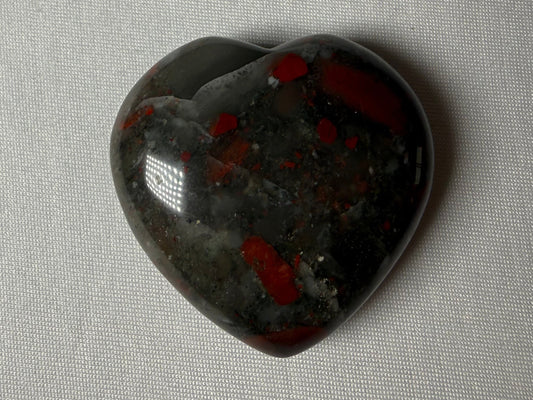 Heart-shaped stone with red and black patterns on a gray fabric background